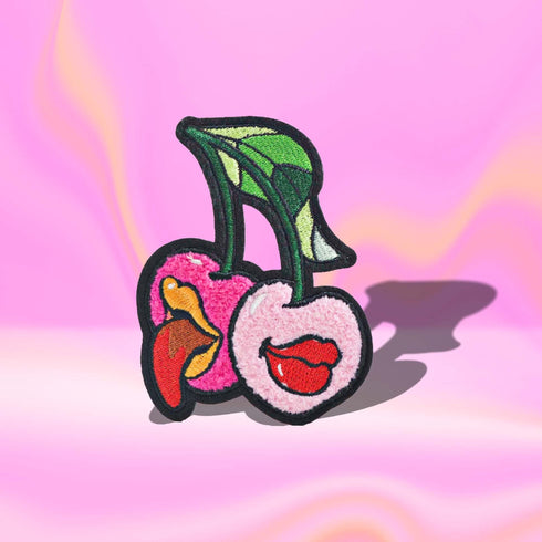 Patch featuring two cherries with expressive lips, one with a tongue sticking out, set against a white background. The design is playful and vibrant, combining bold colors with a fun, cheeky style.